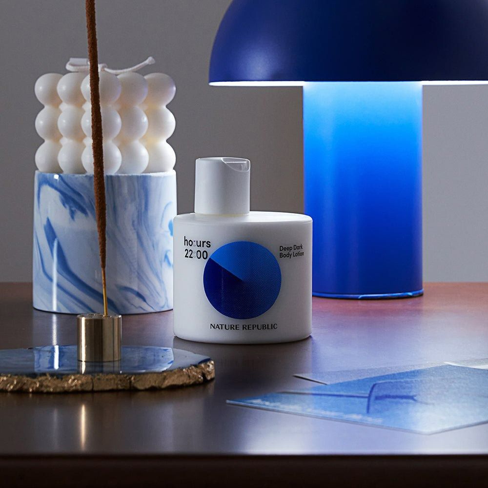 Witte fles met blauwe cirkel. Opschrift: ho:urs 22:00, NATURE REPUBLIC. Op tafel met kaars en lamp.