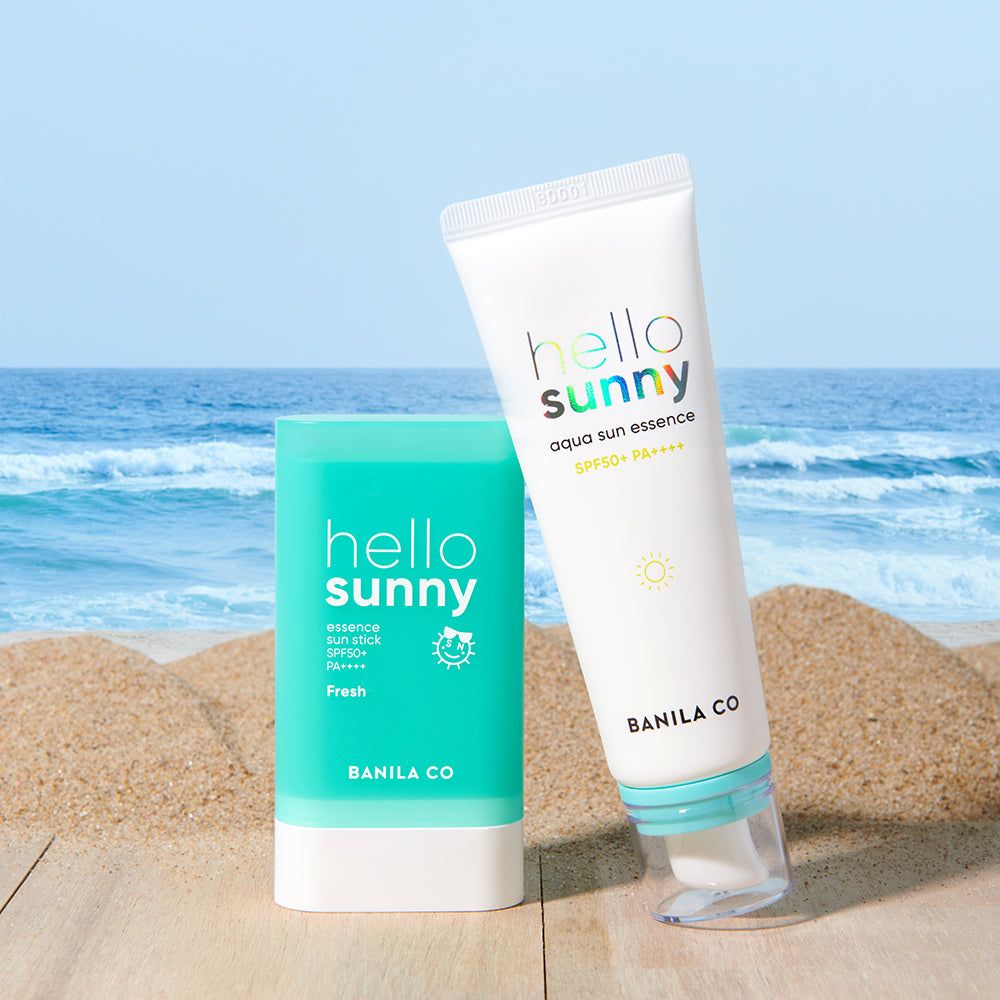 Twee Banila Co. Hello Sunny zonneproducten: een tube zonne-essence en een zonne-stick op een strandachtergrond.