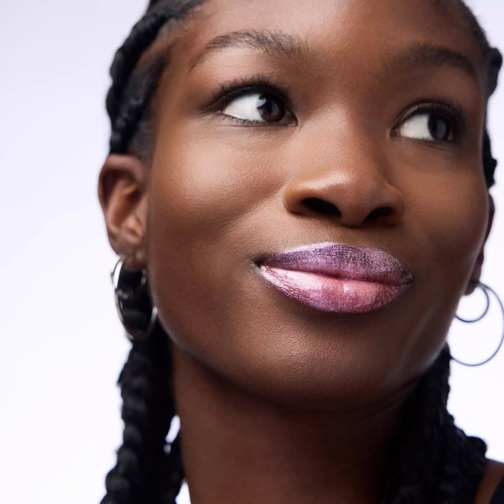 Close-up van een vrouw met roze glanzende lipgloss op haar lippen. Ze draagt zilveren oorringen.