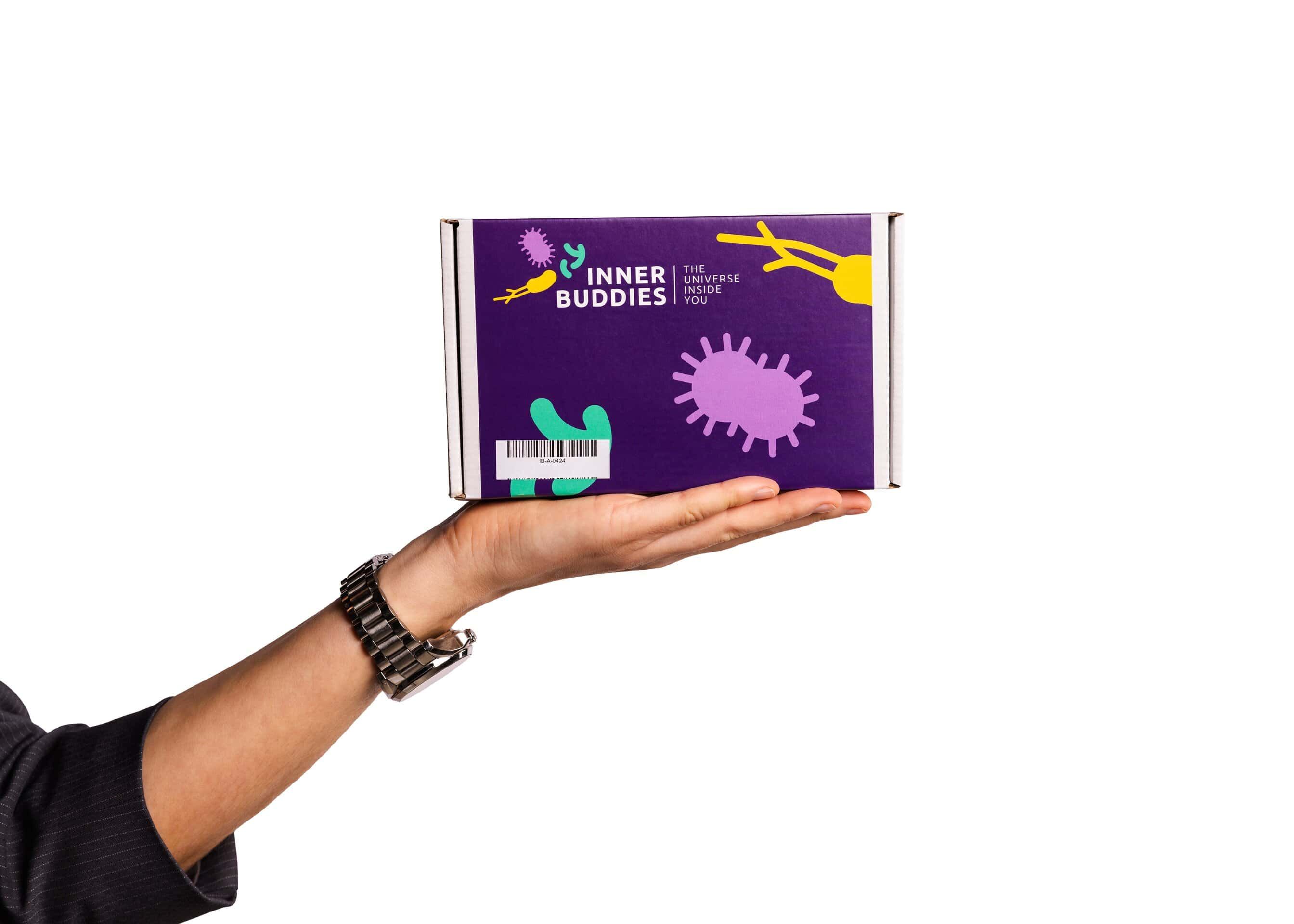 Inner Buddies Microbioom testkit verpakking, in een hand gehouden, met kleurrijke microbe-illustraties.