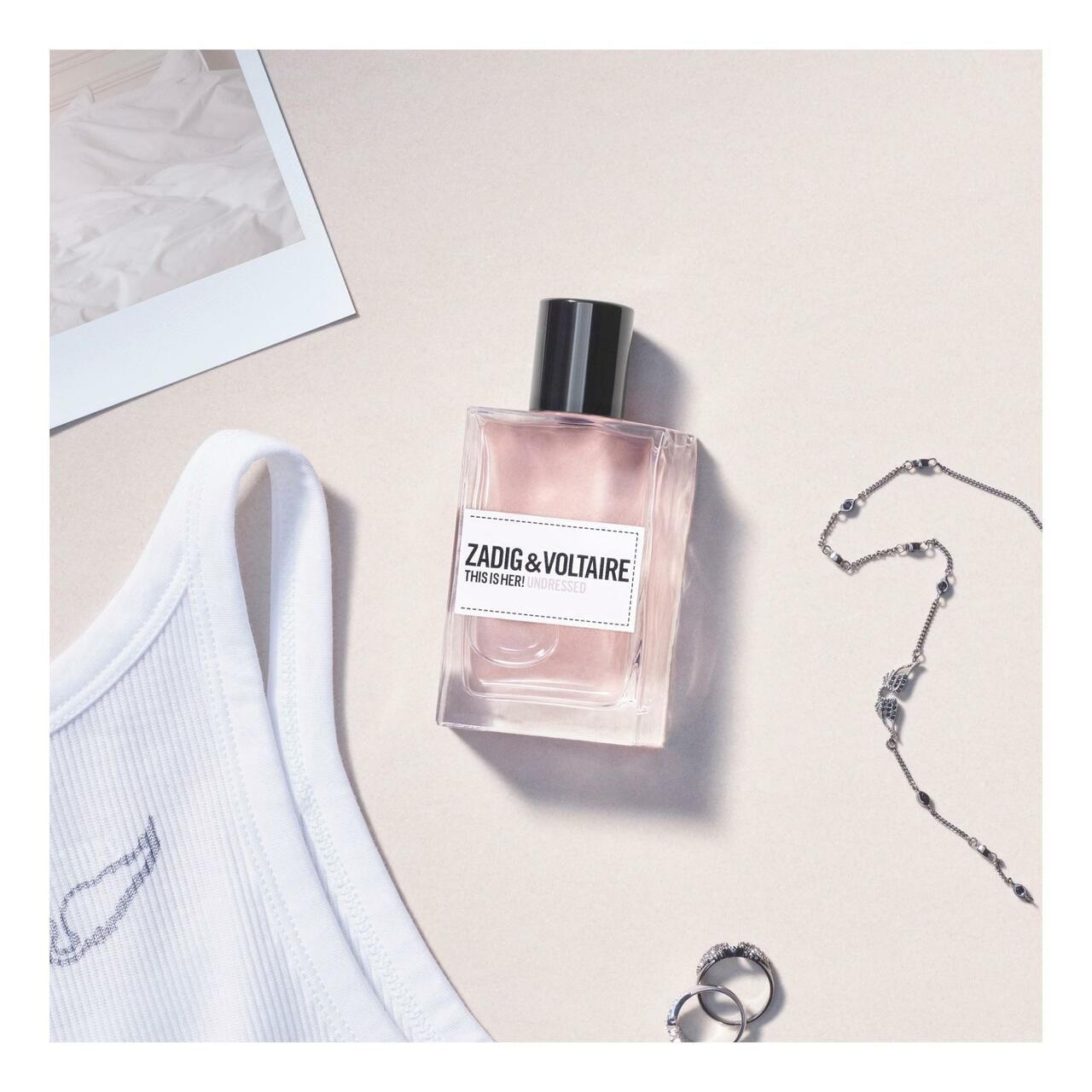 Zadig & Voltaire This Is Her! Undressed Eau de Parfum. Rechthoekige fles met roze vloeistof. Op lichte achtergrond met accessoires.