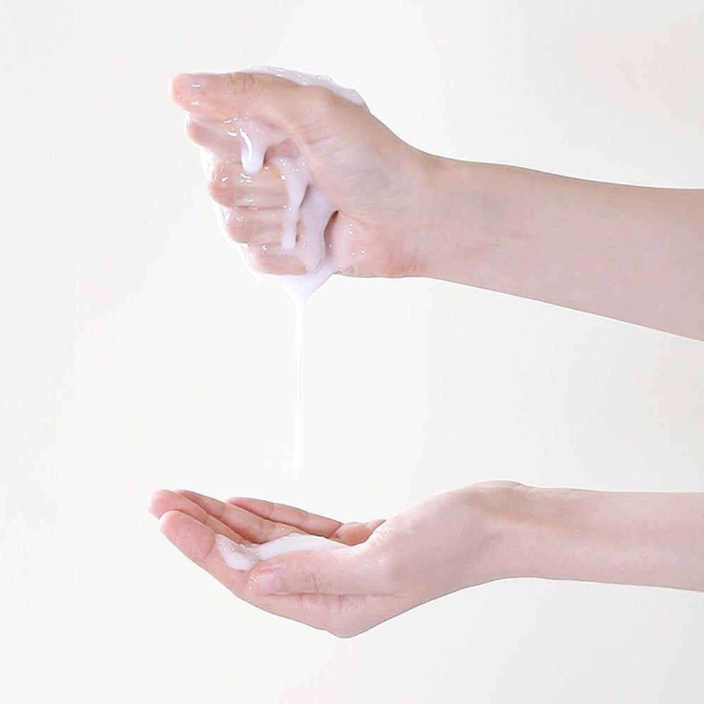 Handen die een witte, vloeibare substantie vasthouden. Vloeistof druppelt in de onderste hand.