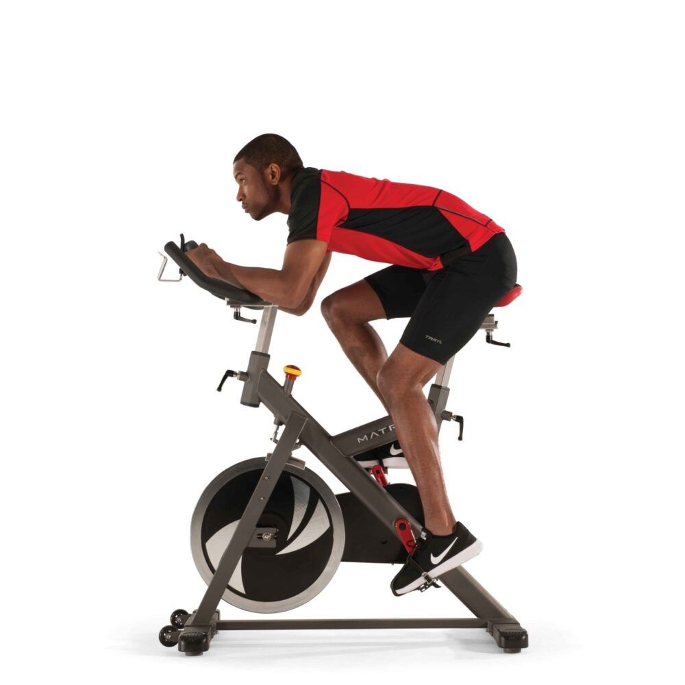 Indoor Cycle. Grijs frame, zwart stuur, rood zadel. Persoon aan het trainen. Persoon in trainingspositie.