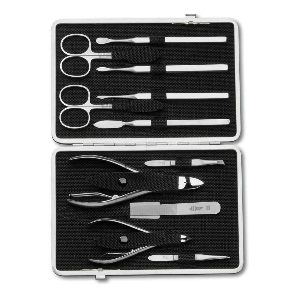 Trousse de manucure ouverte, étui argenté, intérieur noir. Contient ciseaux, limes, pinces et autres outils. Vue de dessus.