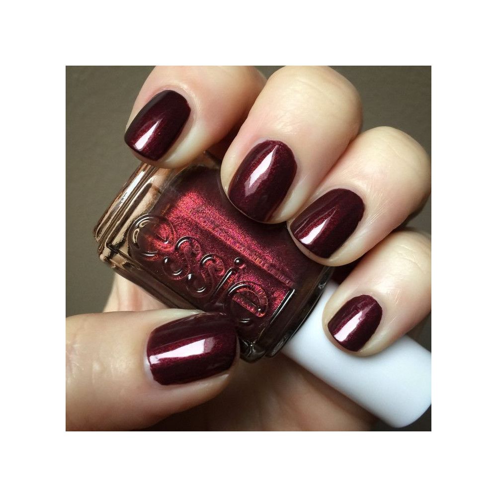 Essie nagellakfles en bordeauxrode gelakte nagels. Transparante fles met logo. Hand met gelakte nagels.