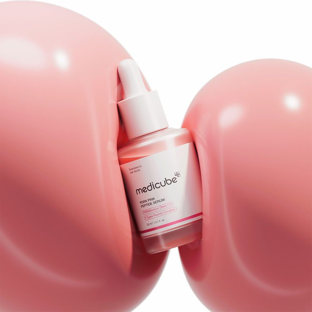 Flacon de Medicube PDRN Pink Peptide Serum entre deux grandes sphères roses.