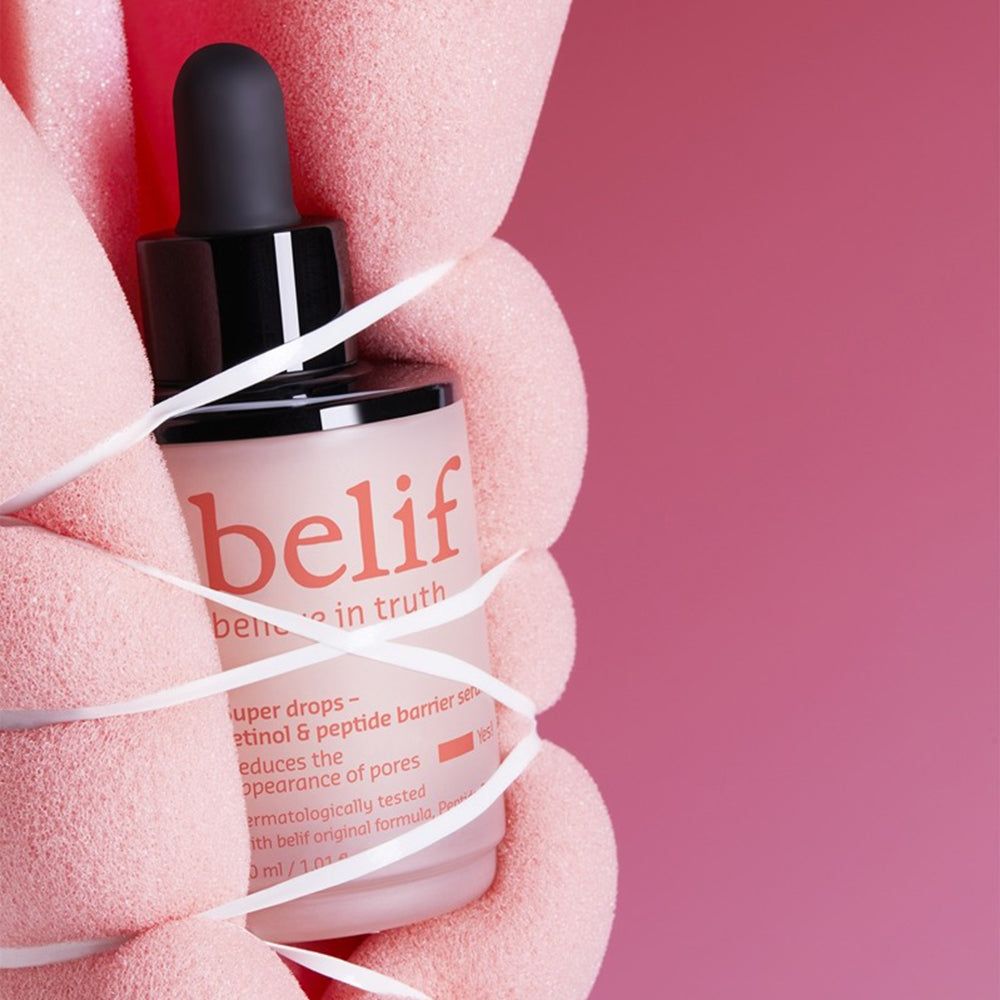 Handen houden Belif Super Drops serumfles vast, omwikkeld met lint.