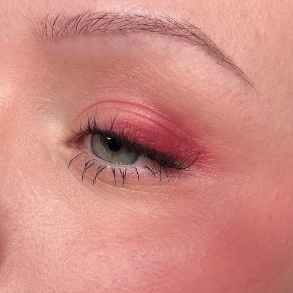 Gros plan sur un œil avec fard à paupières rouge et mascara. Fond de teint.