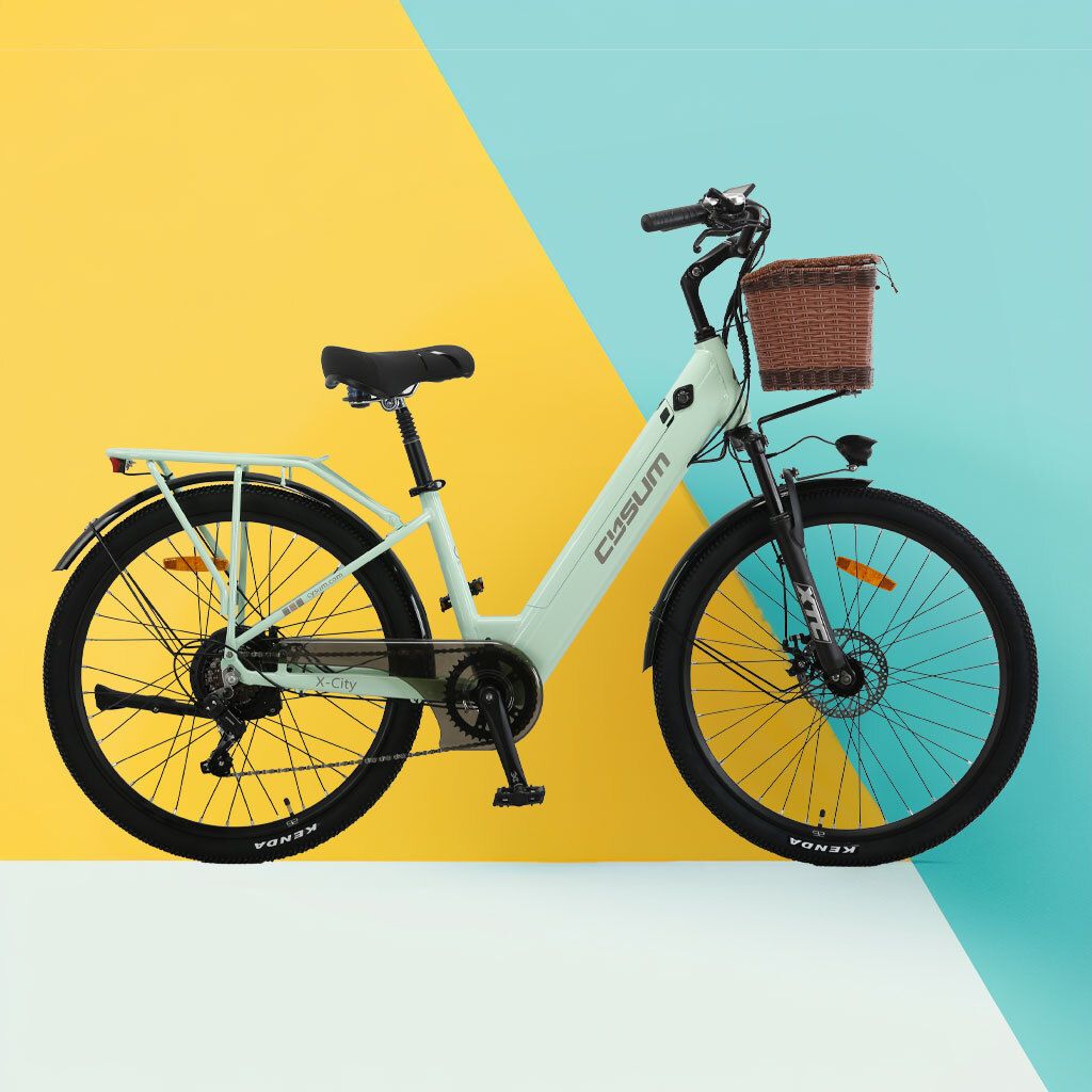 Vélo électrique vert clair avec panier, selle noire et pneus. Fond jaune et bleu.