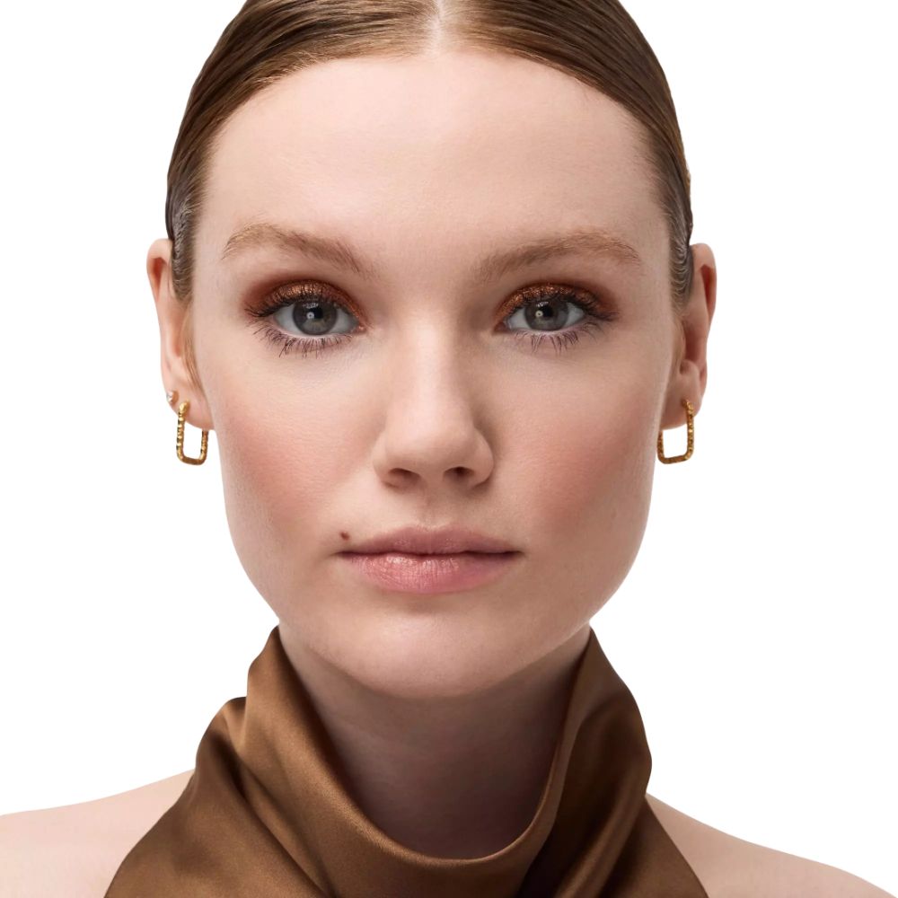Close-up van een gezicht met gouden oogschaduw. De persoon draagt gouden oorbellen. Bruine sjaal.