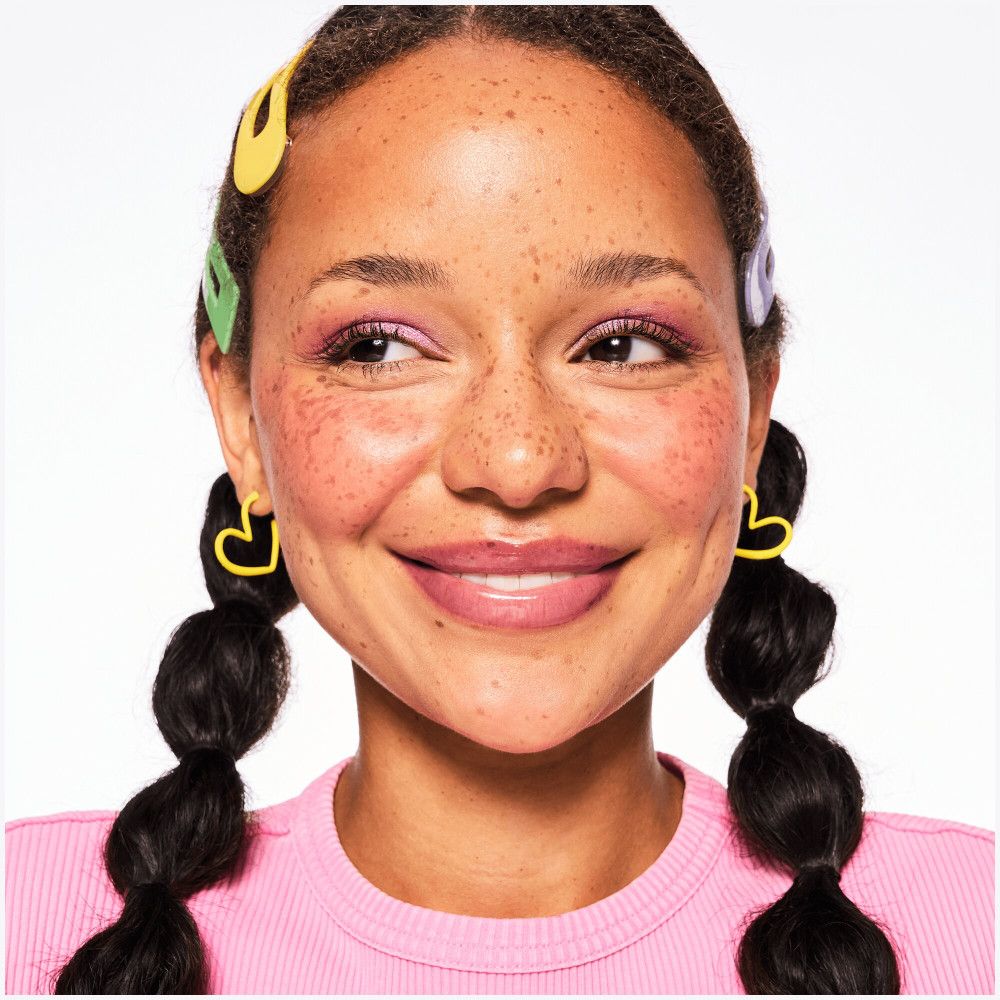 Portret van een vrouw met sproeten en glanzende lippen. Gele hartvormige oorbellen.