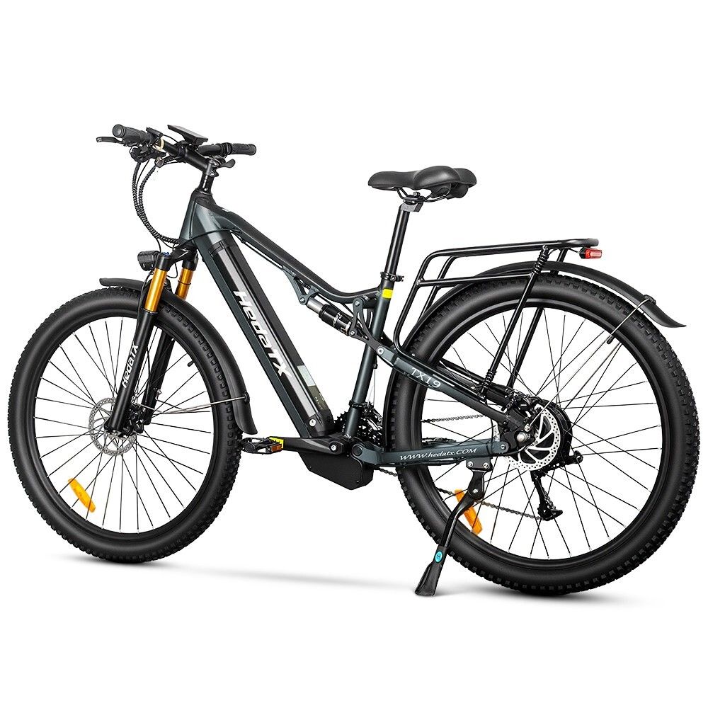 Vélo électrique gris HedaTX TX19. Pneus noirs, porte-bagages, suspension. Fourche jaune. 27 vitesses. Inscription HedaTX.