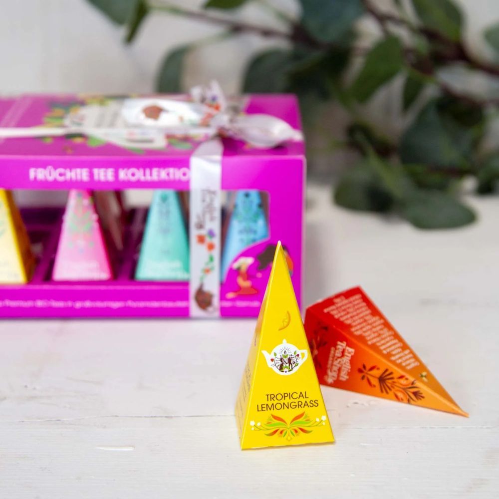 Roze theegeschenkdoos met piramide theezakjes. Twee piramide theezakjes ernaast. Opschrift: Tropical Lemongrass.