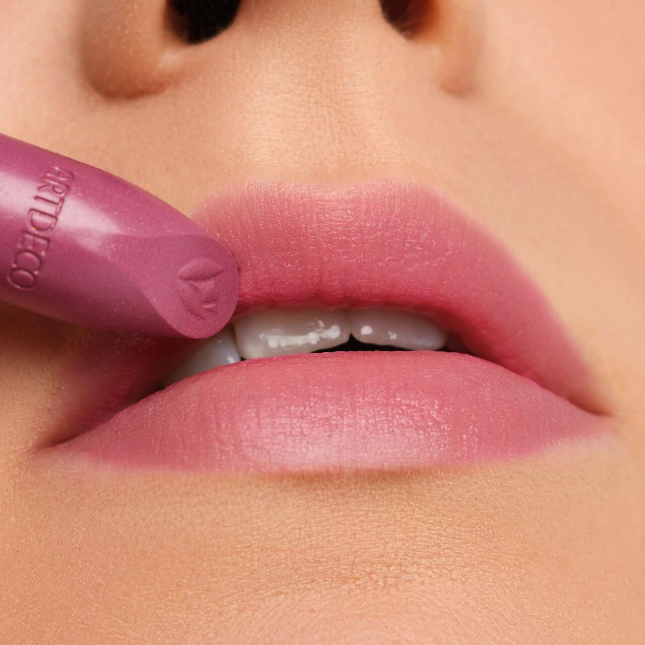 Lipstick wordt op lippen aangebracht. Roze tint. Merk Artdeco zichtbaar. Close-up.
