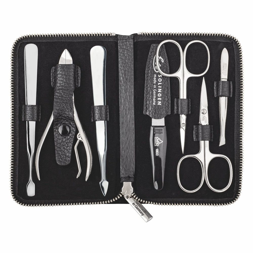 Étui noir ouvert avec 7 instruments de manucure en métal brillant, dont ciseaux, pince à épiler et repousse-cuticules.