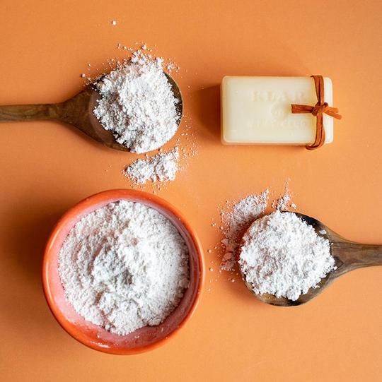 Savon avec ruban, cuillères en bois et bol avec poudre blanche. Sur fond orange. Cuillères et bol contiennent de la poudre.