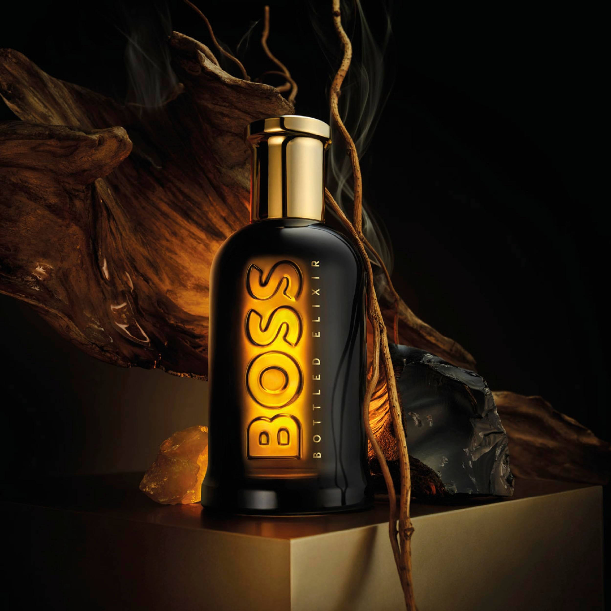 Flacon Hugo Boss Bottled Elixir sur un socle doré, entouré de bois et de pierre.