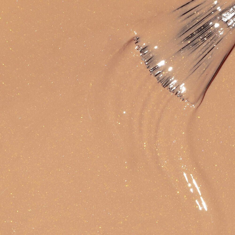Beige nagellak. Penseel dompelt in de vloeistof. Glinsterende deeltjes zichtbaar.