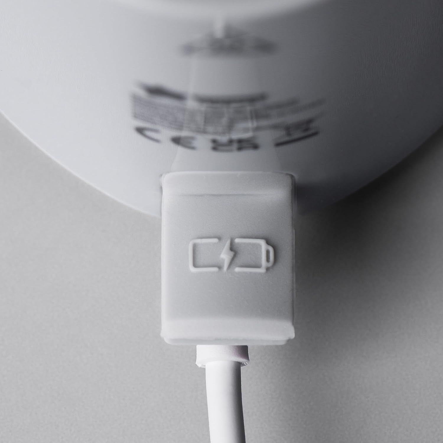 Un port de chargement blanc avec un symbole de batterie et un éclair. Un câble blanc est connecté.