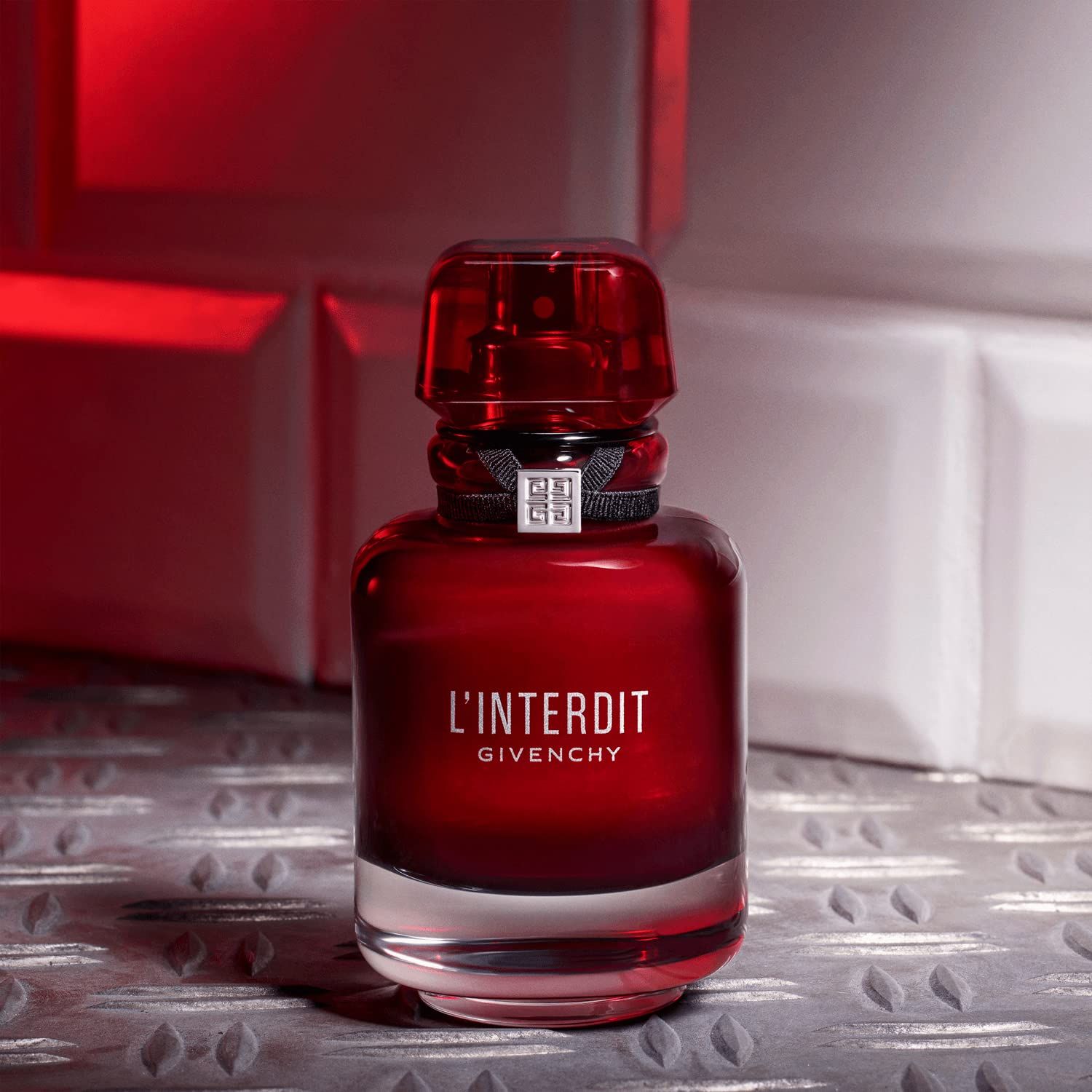Rode fles van Givenchy L'Interdit Eau de Parfum Rouge. Zwart lint met zilveren logo. Op metalen achtergrond.