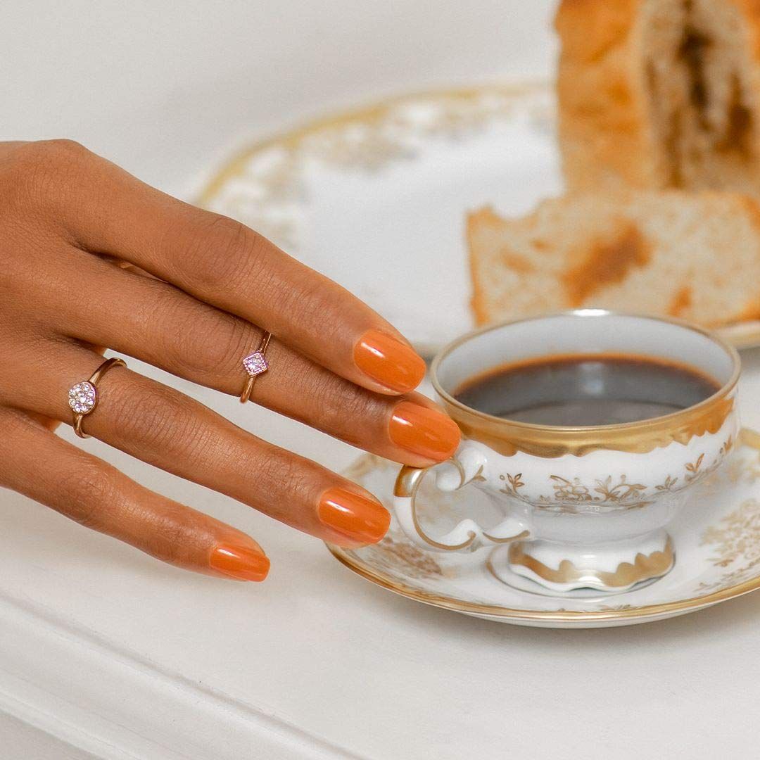 Hand met gelakte nagels, koffiekopje, gebak. Gouden ringen.