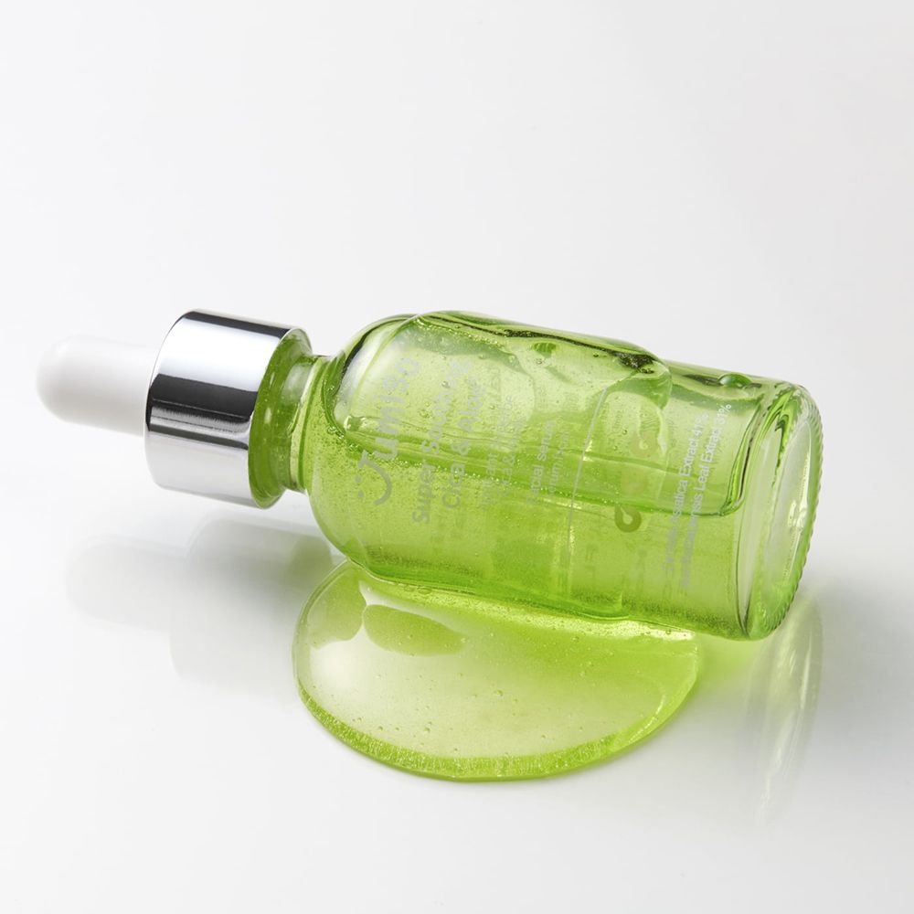 Groene glazen fles met pipet ligt op een wit oppervlak. Daarnaast een kleine hoeveelheid serum.