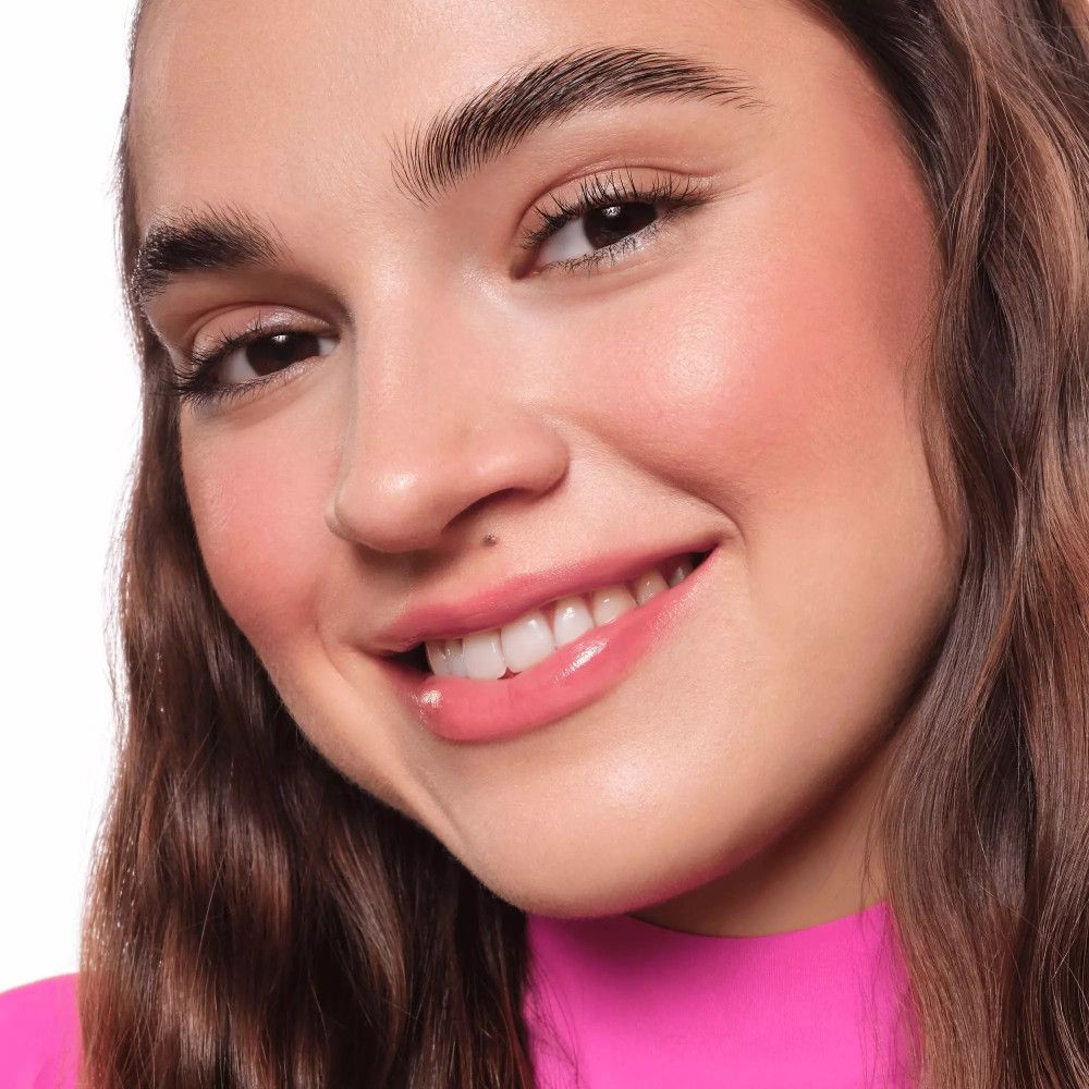 Gros plan d'un visage souriant. La peau est bronzée et brillante. Les lèvres sont roses.