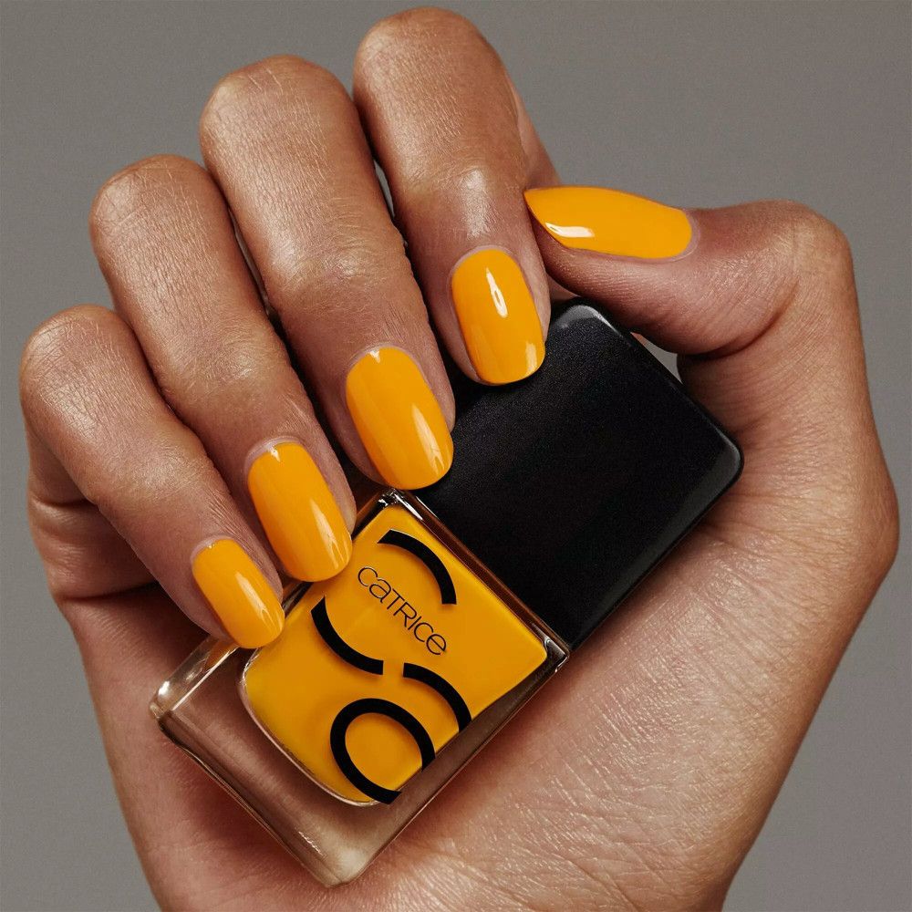 Main avec vernis à ongles jaune et flacon de vernis à ongles Catrice. Flacon avec bouchon noir, contenu jaune et logo Catrice.