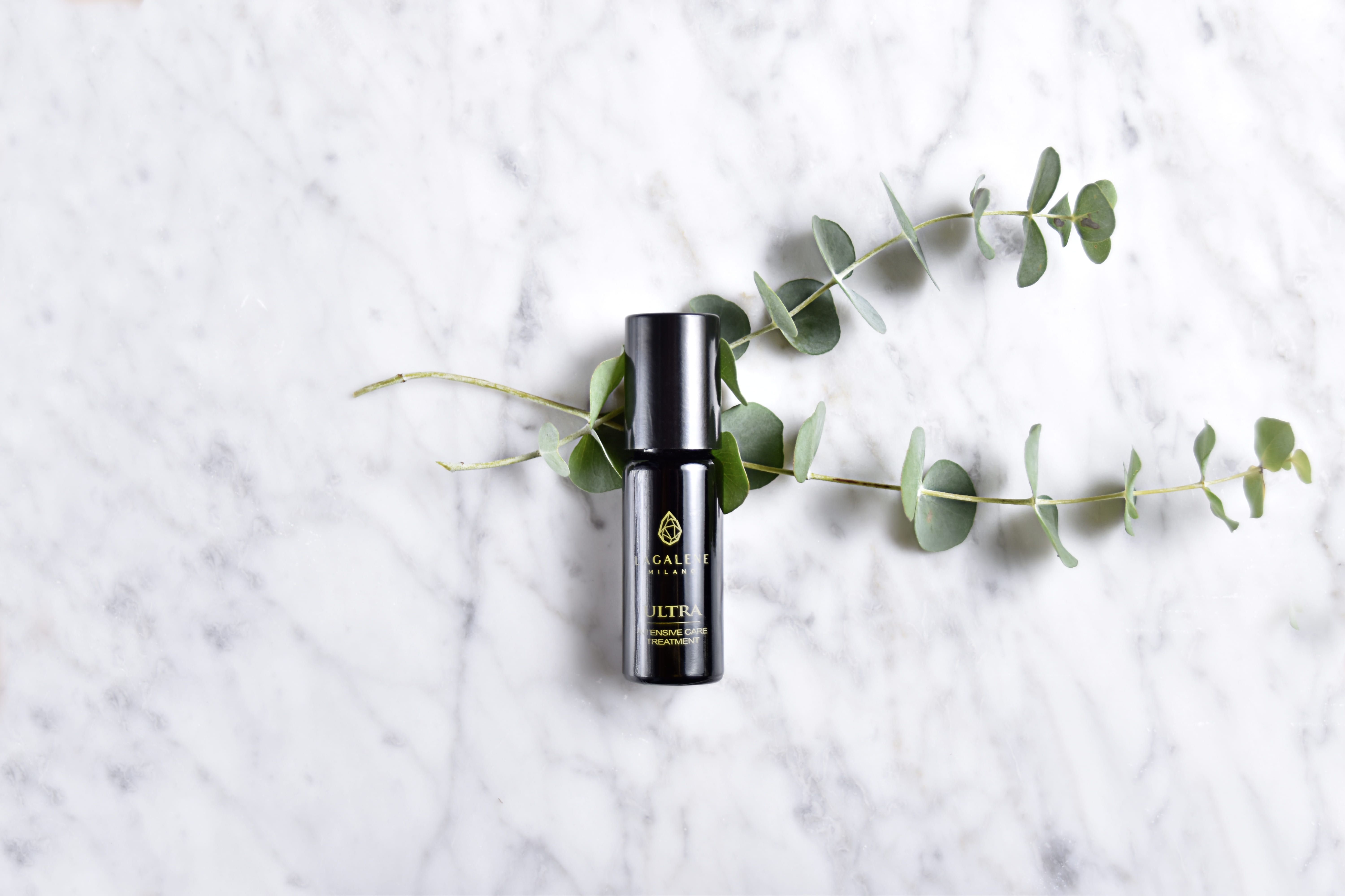 Een Lagalene Milano Ultra Intensive Care fles ligt op een marmeren oppervlak, omringd door eucalyptus takken. Op de fles staat "ULTRA INTENSIVE TREATMENT".