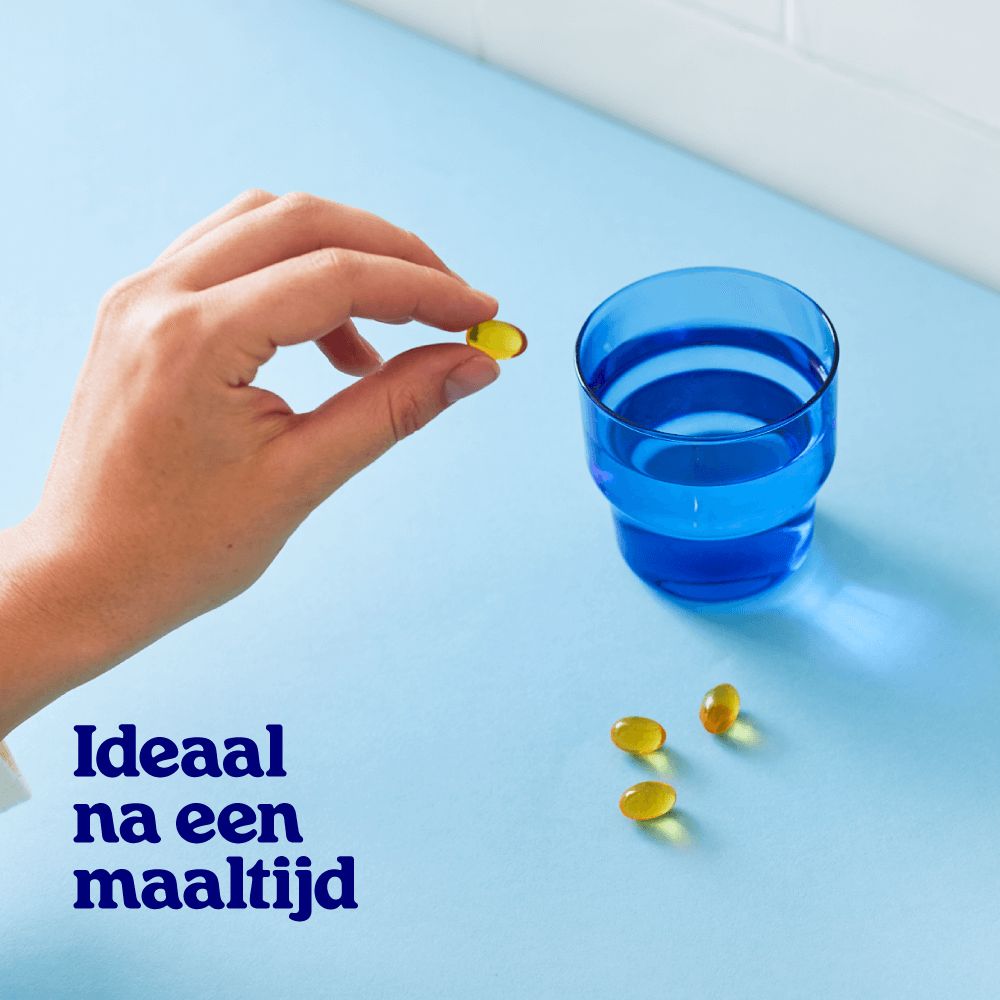 Hand houdt een Omega 3 capsule vast boven een blauw glas water.