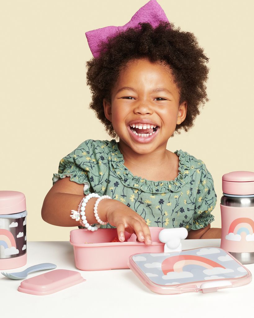 Kind met lunchbox en thermosfles. Roze lunchbox met regenboogontwerp. Thermosfles met regenboogontwerp en lepel.