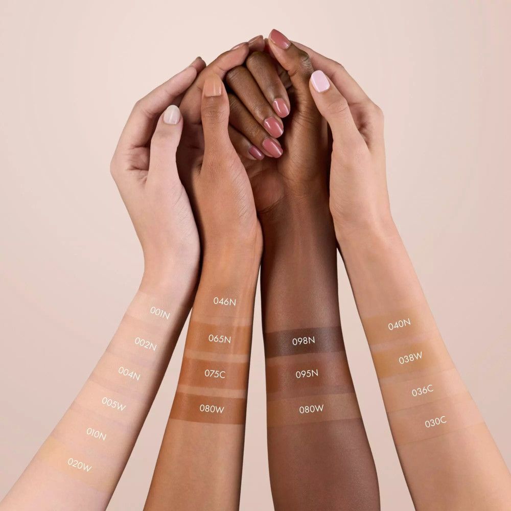 Mains avec différents tons de peau, avec des teintes de Catrice Nude Drop Sérum Teinté Foundation. Numéros de couleurs visibles.