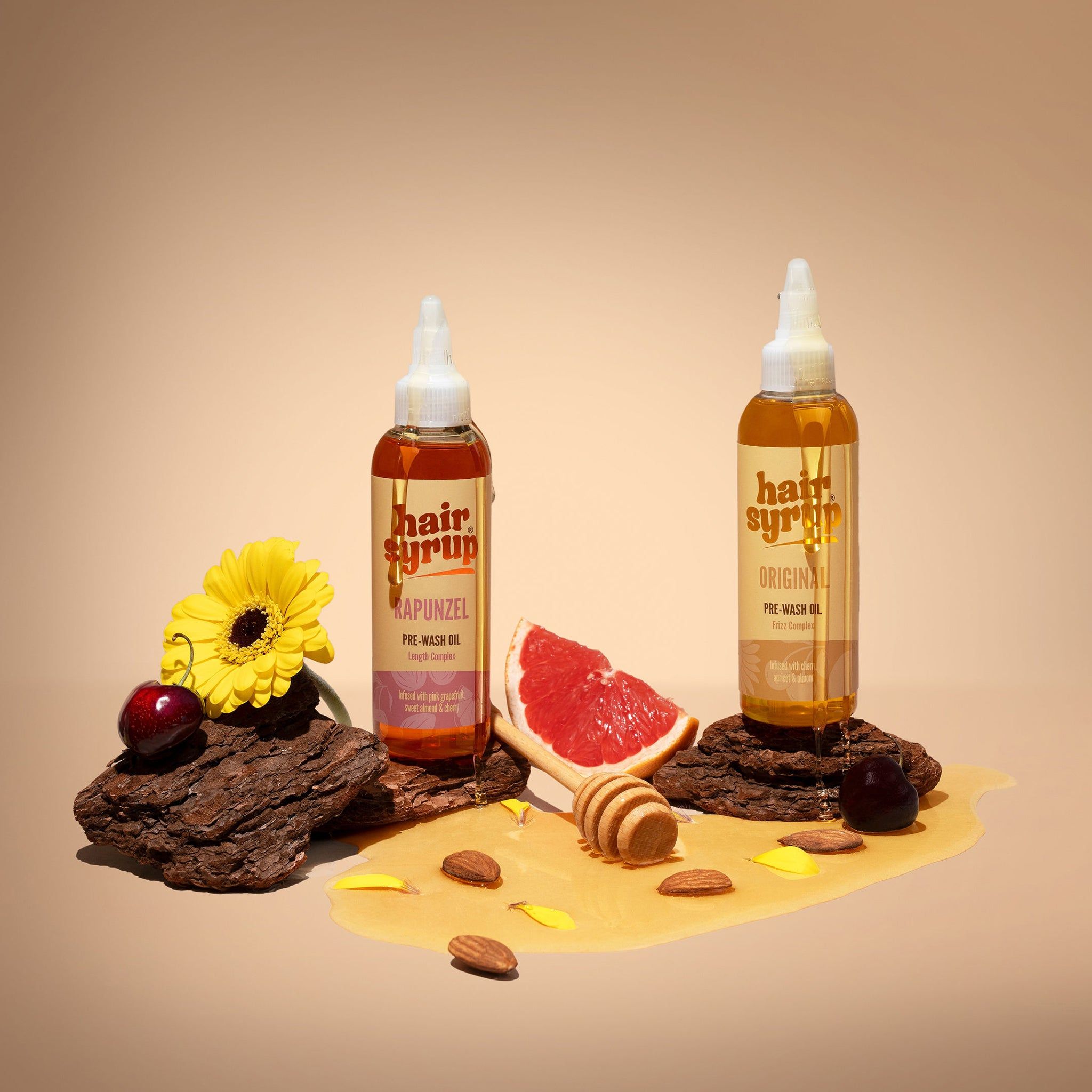 Twee flessen Hair Syrup, één met label 'Original', de andere 'Rapunzel'. Op stukken hout met grapefruit en honing.