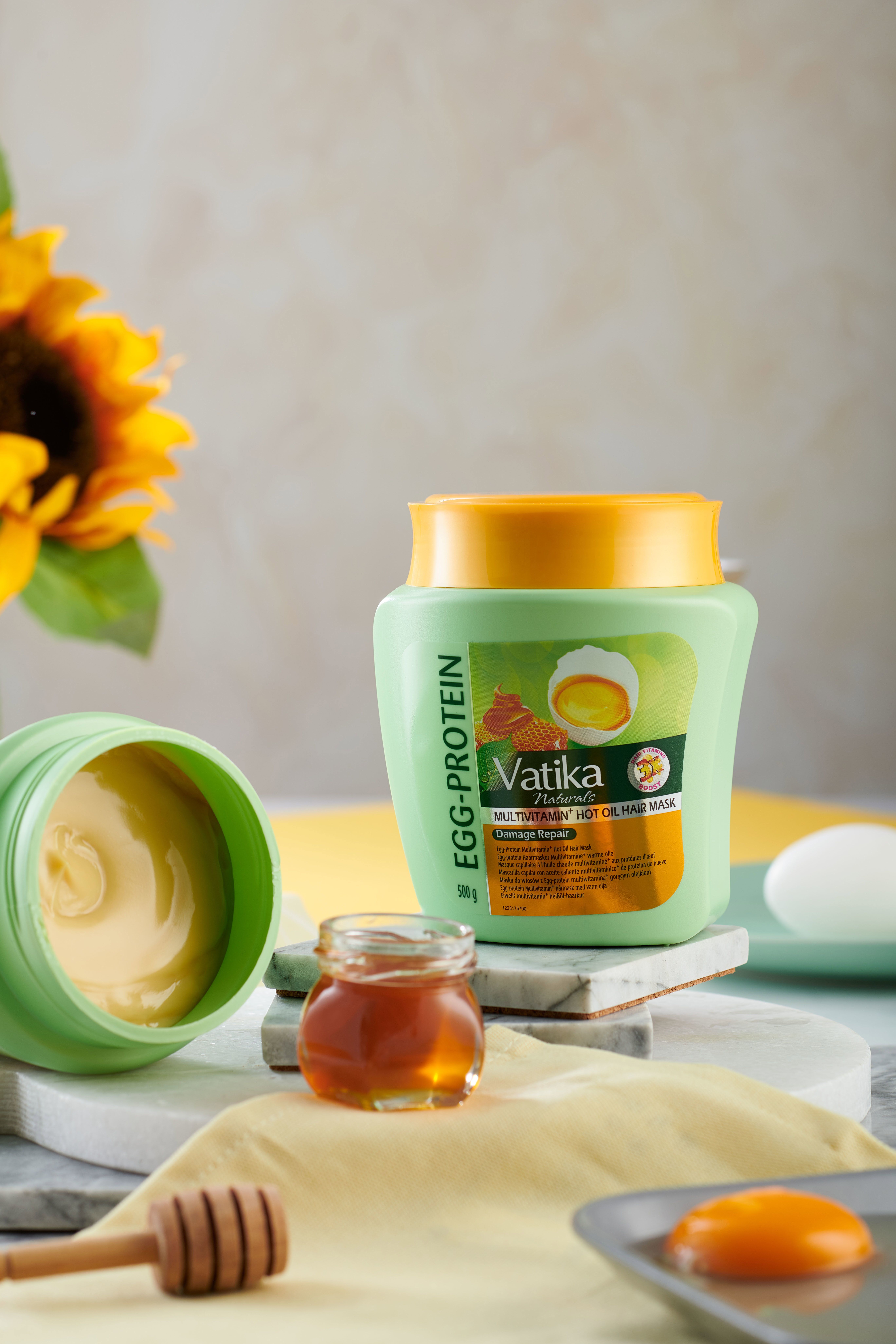 Open groene haarmasker met gele deksel. Honingpot, eierschalen, houten stok. Tekst: Vatika Naturals, Egg-Protein, Multivitamin, Hot Oil Hair Mask.