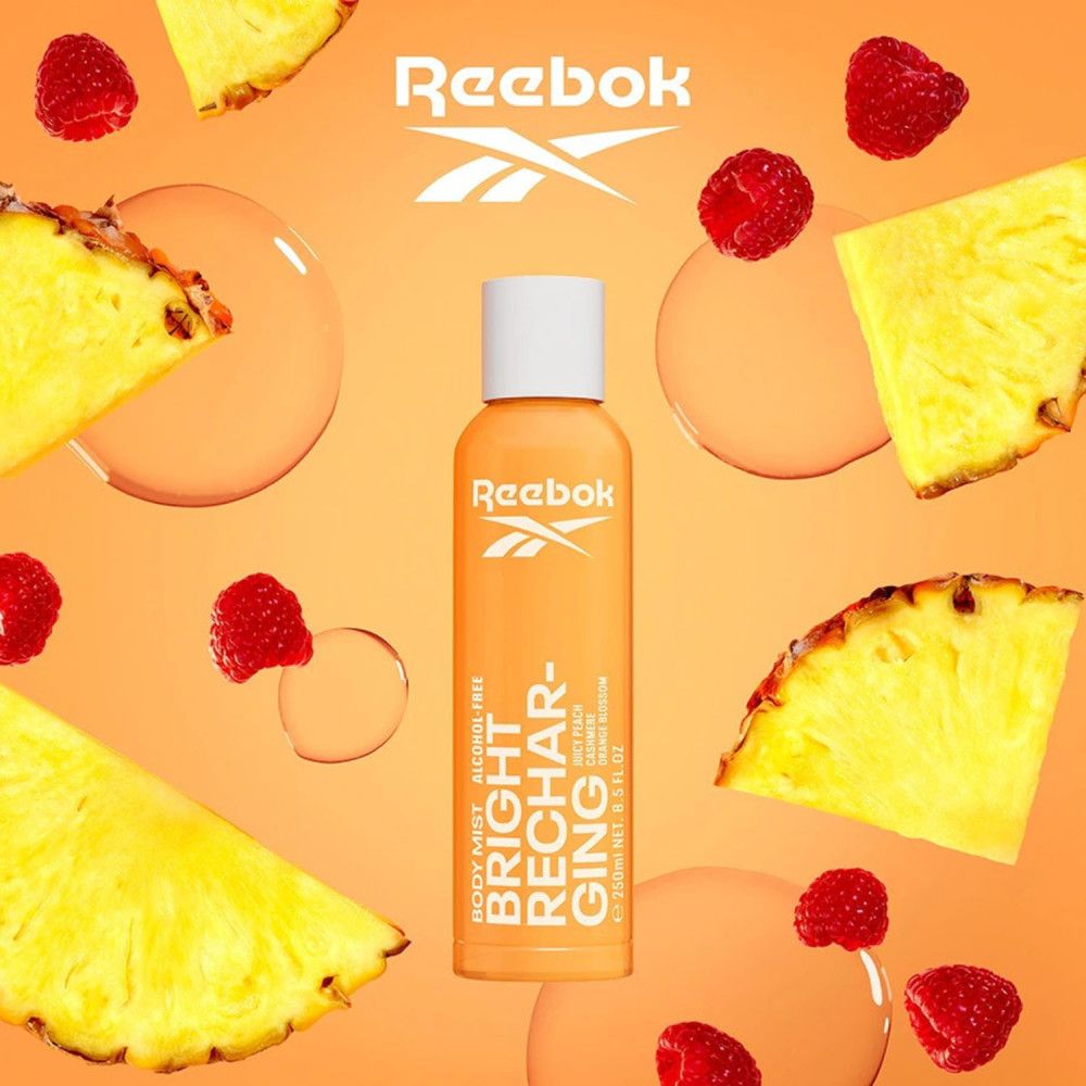 Oranje fles met witte dop. Tekst: Reebok, Bright Recharging. Omringd door stukjes ananas en frambozen.