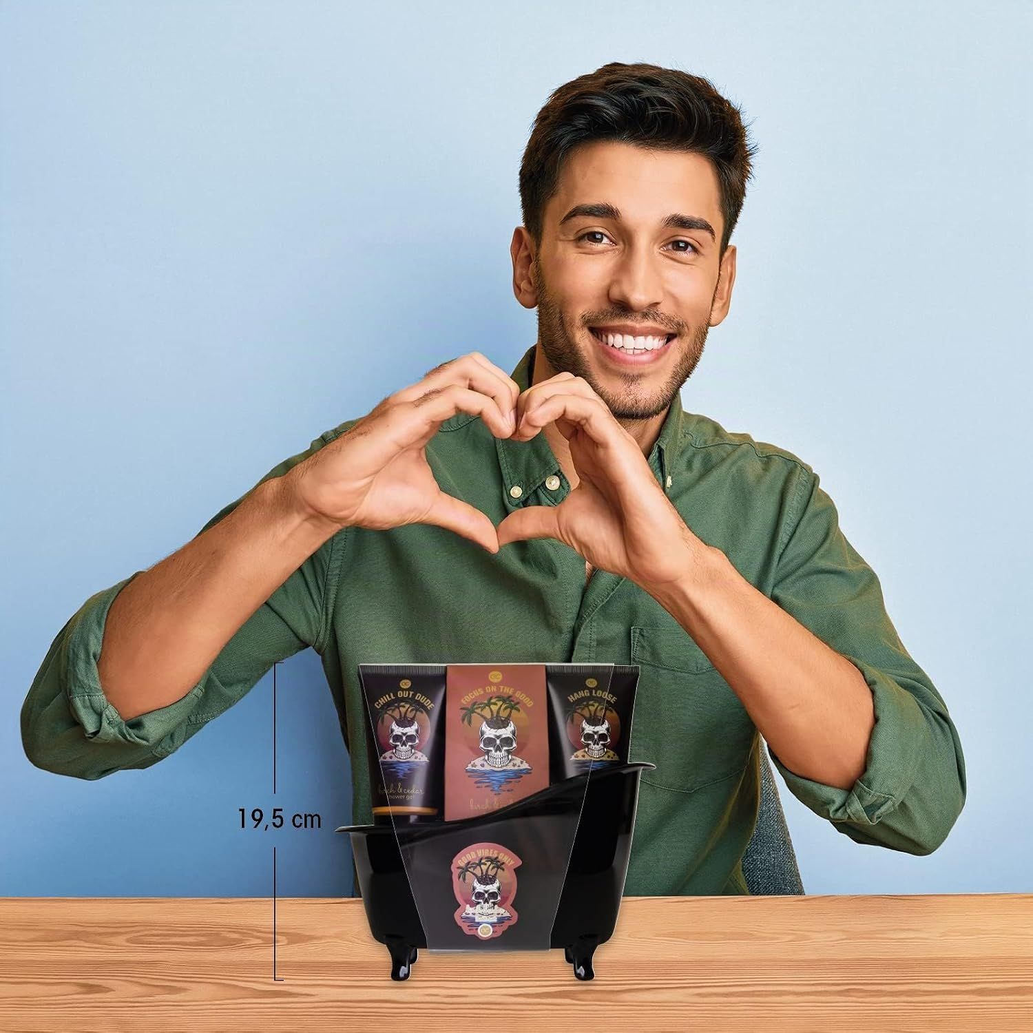 Un homme forme un cœur avec ses mains au-dessus d'un panier cadeau noir contenant trois tubes et une boîte.