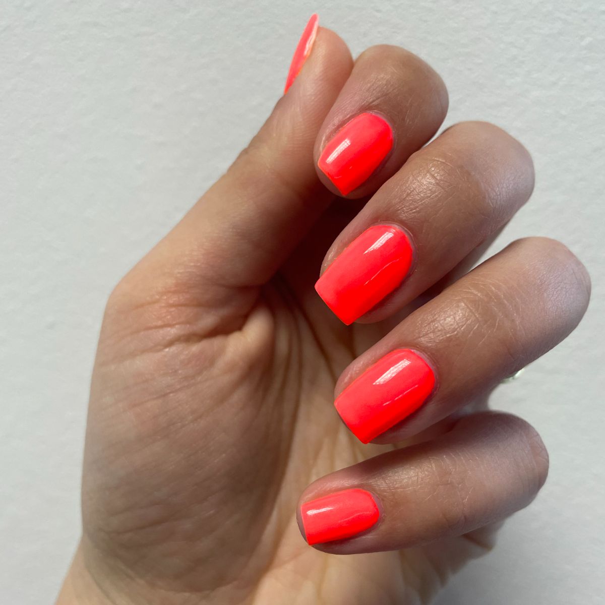 Main avec ongles orange néon. Les ongles sont courts et carrés.