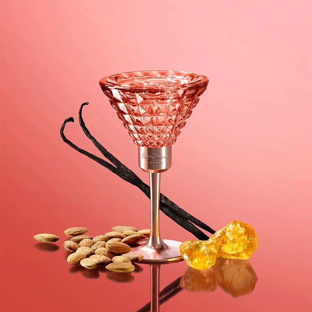 Parfumfles in kelkvorm. Roze glas met geometrisch patroon. Vanillestokjes, amandelen en amberkleurige stukjes ernaast.