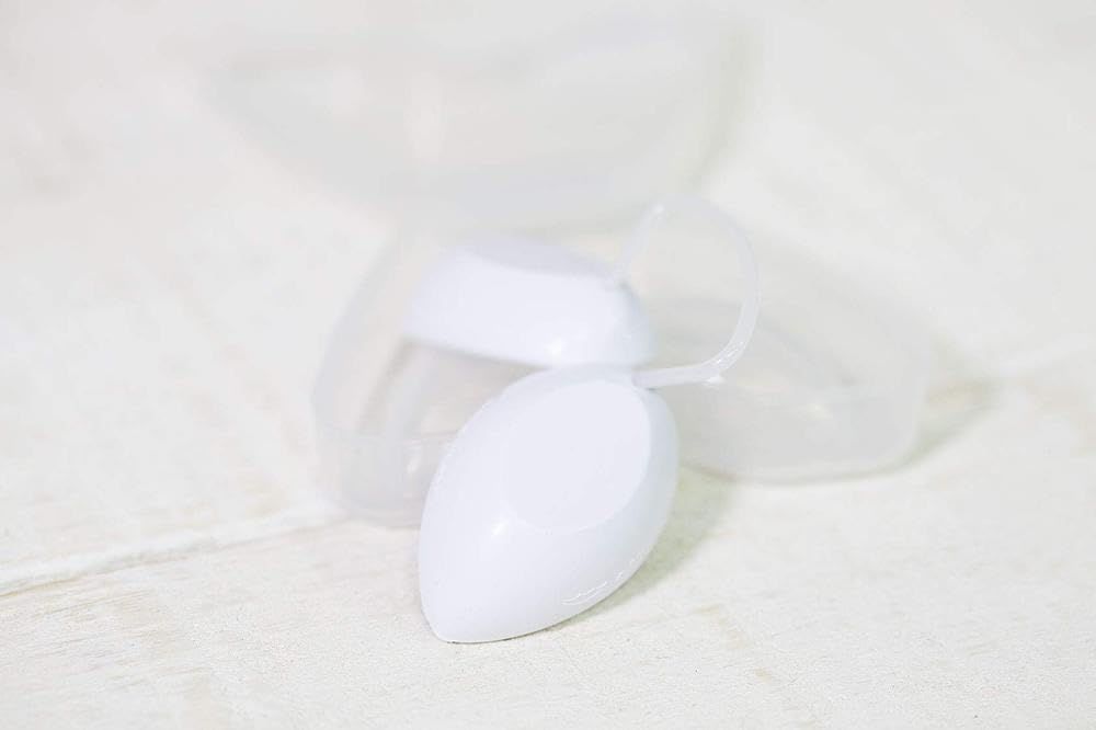 Produit blanc ovale dans un étui transparent en deux parties. Le produit est devant l'étui ouvert.