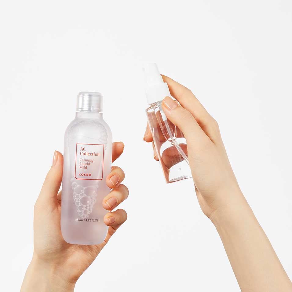 Twee handen houden fles en sprayfles. Fles met rood etiket: AC Collection, Calming Liquid Mild, COSRX. Transparante vloeistoffen.