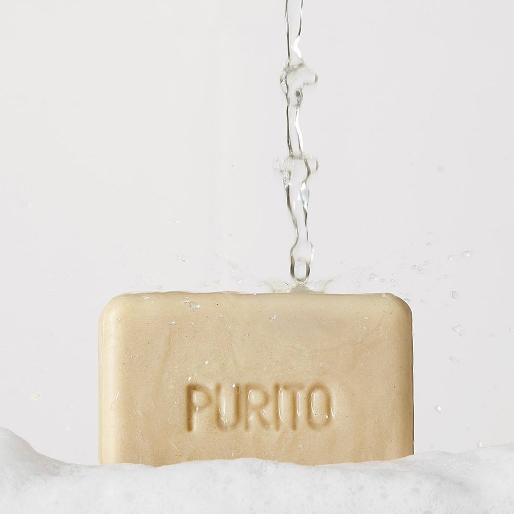 Savon beige dans de la mousse, de l'eau est versée dessus. Le mot "PURITO" est visible.