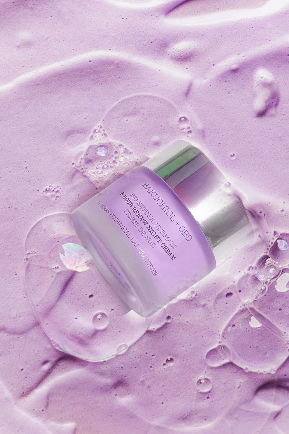Pot de crème avec couvercle argenté, partiellement immergé dans une mousse violette. Inscription : Bakuchiol + CBD, Bio-Retinol Ultimate, 8-Hour Renew Night Cream.