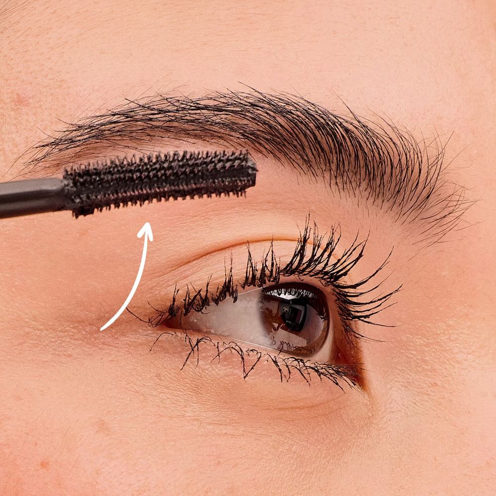 Close-up van een oog. Mascaraborstel wordt op de wimpers aangebracht. Pijl geeft richting aan.