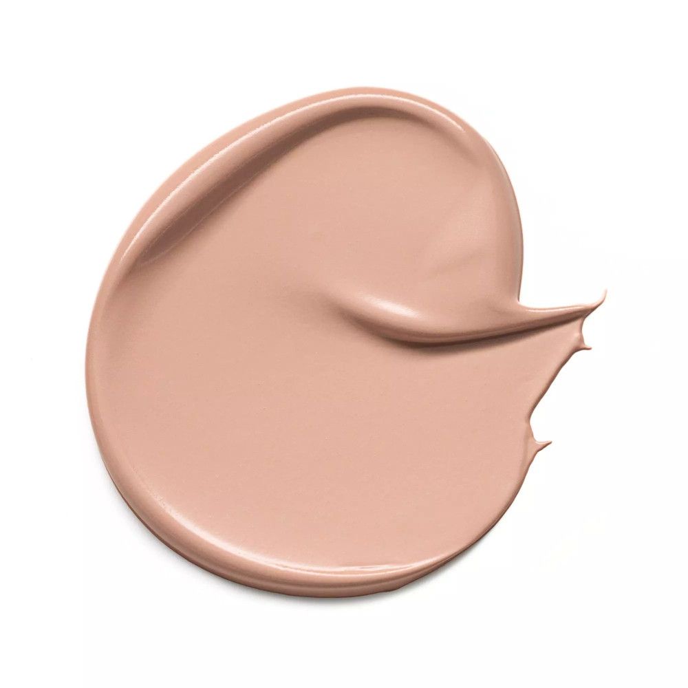 Tache de correcteur beige étalée sur fond blanc. Texture lisse.