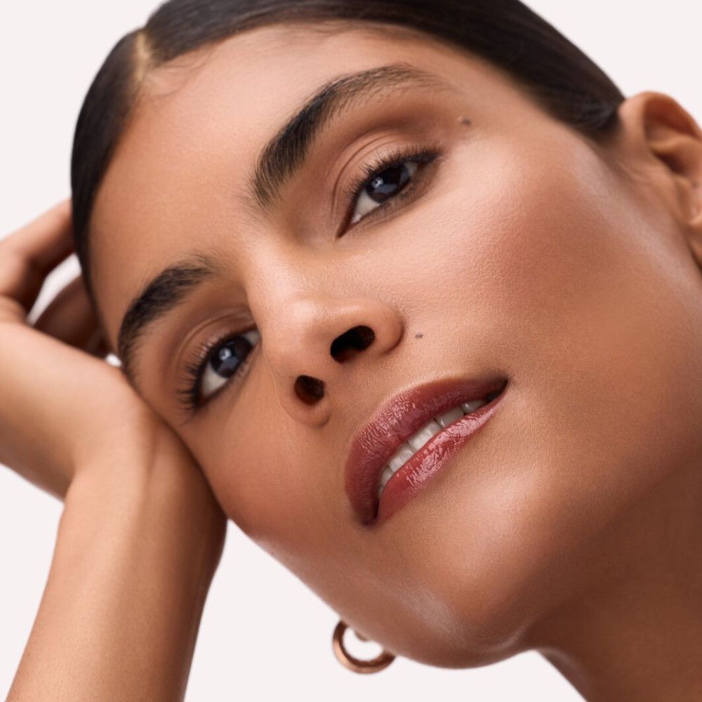 Portret van een vrouw met lip tint op haar lippen. Ze steunt haar hoofd op haar hand, draagt gouden oorringen.