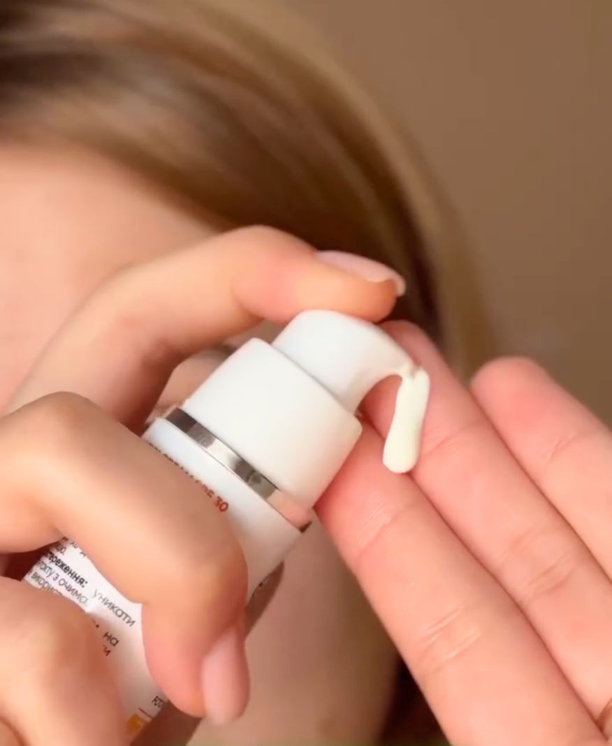 Crème solaire pressée d'un flacon blanc avec pompe sur la main.