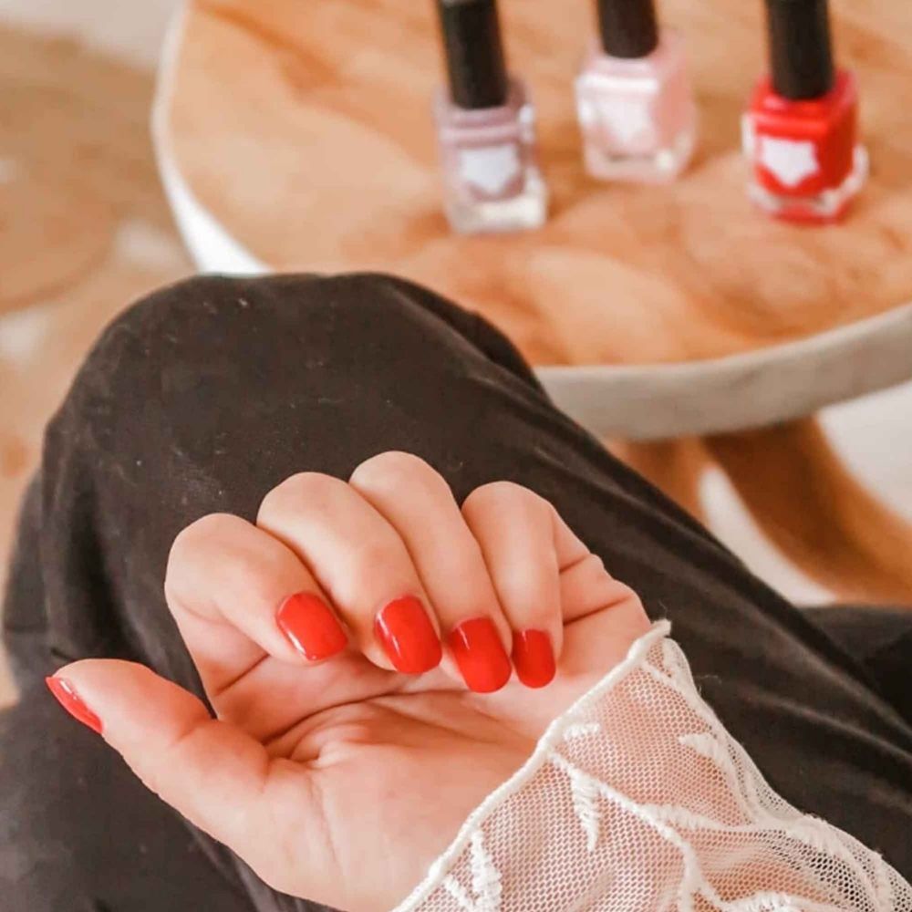 Hand met rode nagels. Op de achtergrond: drie nagellakflesjes.