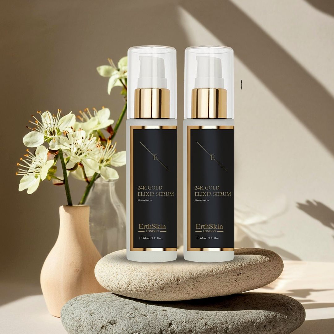 Deux flacons de sérum avec pompes dorées et étiquettes noires. Inscription : 24K Gold Elixir Serum, ErthSkin London. Sur des pierres.