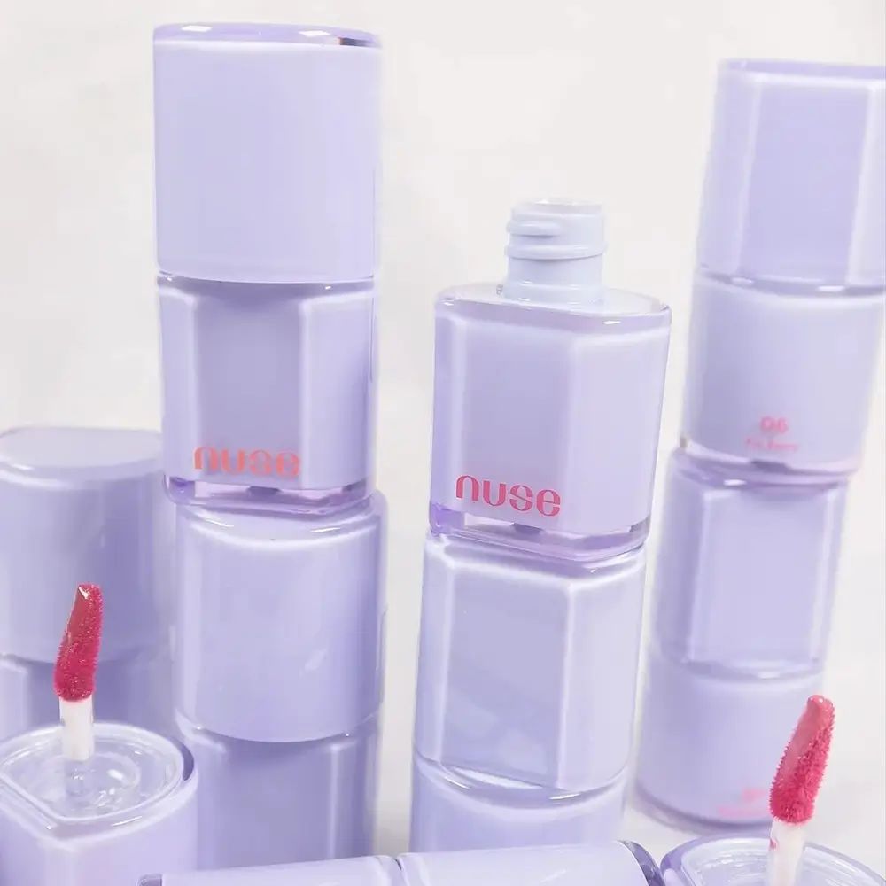 Meerdere flesjes lipgloss. Flesjes bestaande uit twee paarse cilinders met de tekst "nuse" in oranje.