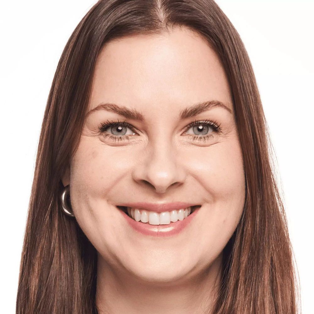 Portrait d'une femme aux cheveux bruns. Elle sourit. Elle porte des boucles d'oreilles.